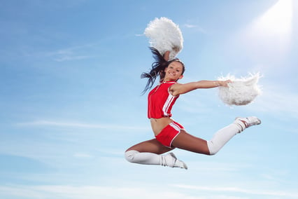 Young beautiful female cheerleader in uniform jumping high