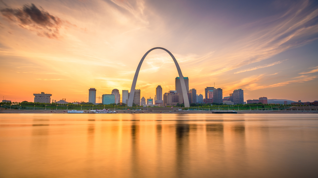 St. Louis skyline at sunset with the Gateway Arch in the center, reflecting over the Mississippi River. Text overlay reads, “Can an Elevation Certificate Save You $1,000 on Flood Insurance?”—highlighting a cost-saving strategy for flood insurance in Missouri.