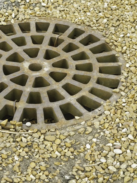 Round storm drain, off center, surrounded by garden stones