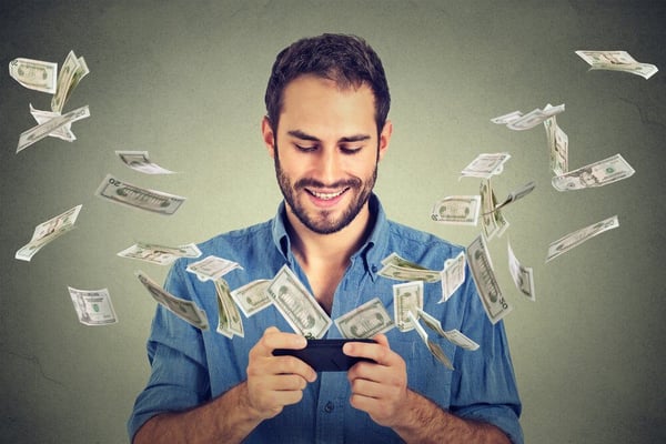 Technology online banking money transfer, e-commerce concept. Happy young man using smartphone with dollar bills flying away from screen isolated on gray wall office background.-1