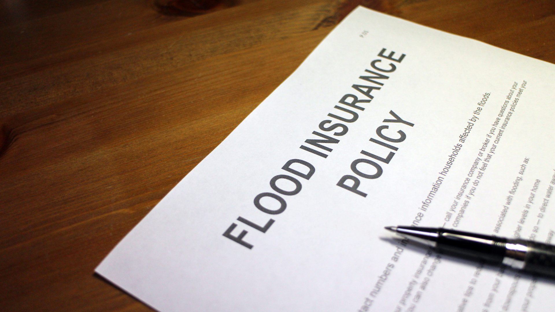 Flood insurance policy document on a wooden table with a pen, representing flood insurance coverage, policy review, and risk protection.