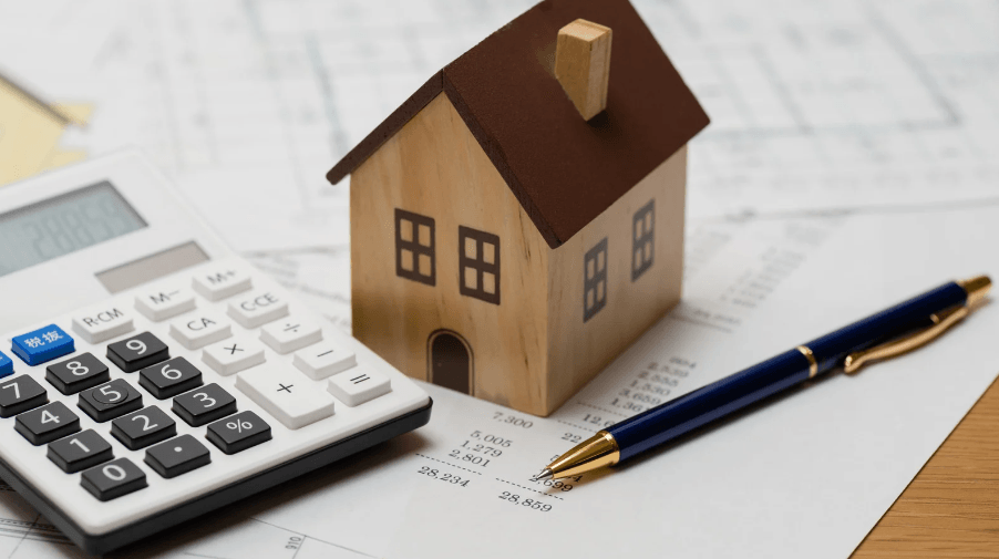 closeup photo of a desk with calculator, a small house, and black pen showing costs