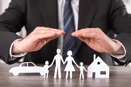 Insurance agent cupping hands over paper family cutouts representing personal asset protection