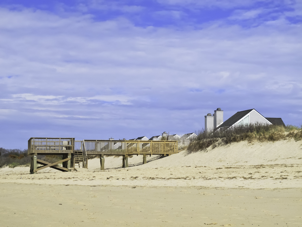 Coastal landscape Beach view of boardwalk and deck by dune near peaked roofs of houses in Cape Cod, Massachusetts-1